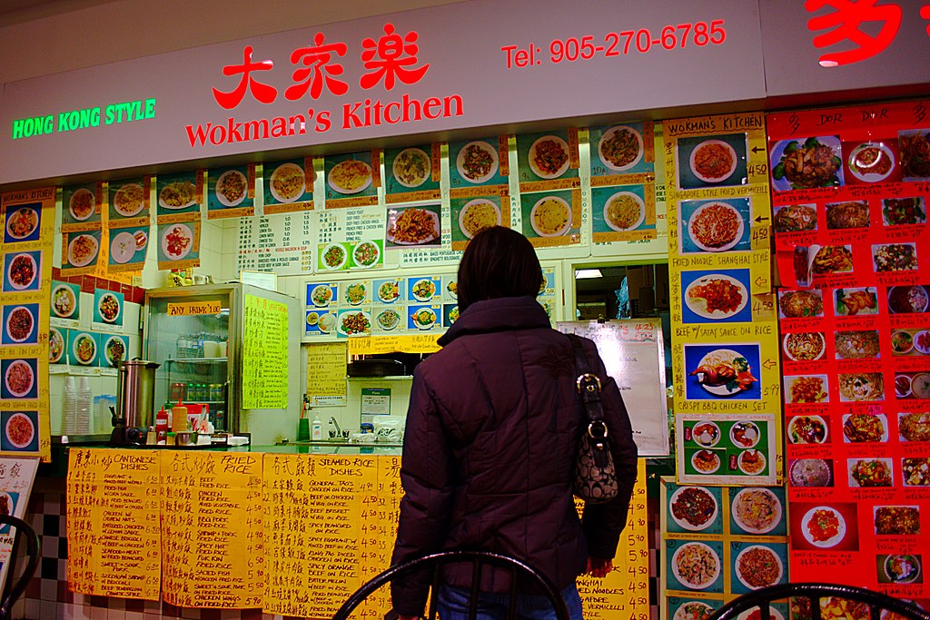 Photograph of the backside of a customer in front of a Hong Kong restaurant with overwhelming menu options that take dozens of images, posters, and signage to explain