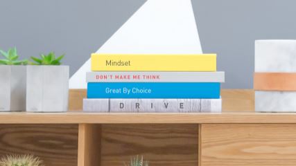 Three books stacked on a shelf surrounded by plants.