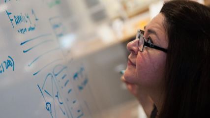 A square image of Cynthia starring up at a whiteboard.