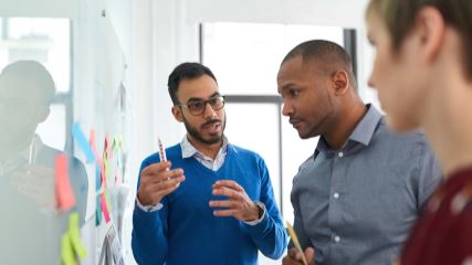 Three people holding a discussion at a whiteboard