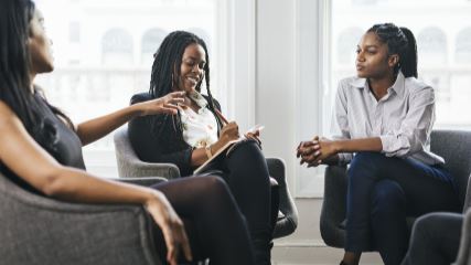 Three people holding a discussion in black chairs