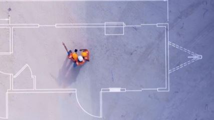 Construction workers standing on blueprints drawn on concrete.