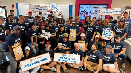 Entire BE team gathered in a colorful room holding signs from Kids' meals talking about the amount of meals we prepared
