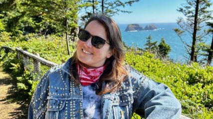 Emily standing outside in front of some trees and a coastline