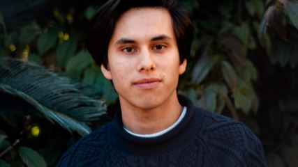 A close-up photo of Krzysztof wearing a blue sweater on a background of green foliage