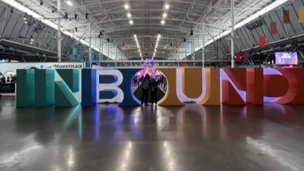 A photograph of Taylor and Chris standing in front of massive block letters spelling out "INBOUND" at the 2024 Inbound conference in Boston.
