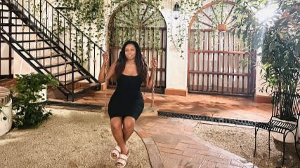Denajia sitting in a courtyard on a rope swing, with green foliage behind her