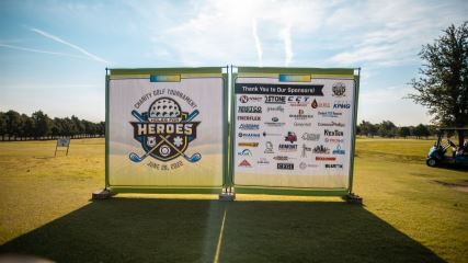 Large panel with charity event graphics on a golf course with sun shining in the background