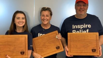 Maeghan, Laura E and Donovan standing in front of a frosted glass window holding their awards for the Chili Cookoff