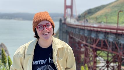 Haley wearing a yellow jacket and an orange beanie in San Francisco with the golden gate bridge in the background