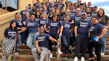 A photo of the entire BrandExtract team wearing navy-blue tshirts with "Inspire Belief" on them, posing on a staircase outside