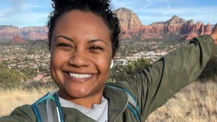 Kameshia wearing a green jacket on a mountain in front of a huge vista with orange and brown mesas