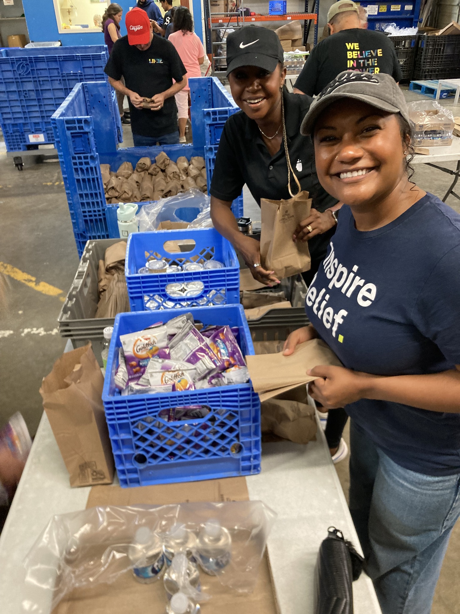 Kammie and Charity smiling as they pack sandwhiches at Houston Kidz Mealz during a volunteer event with BrandExtract