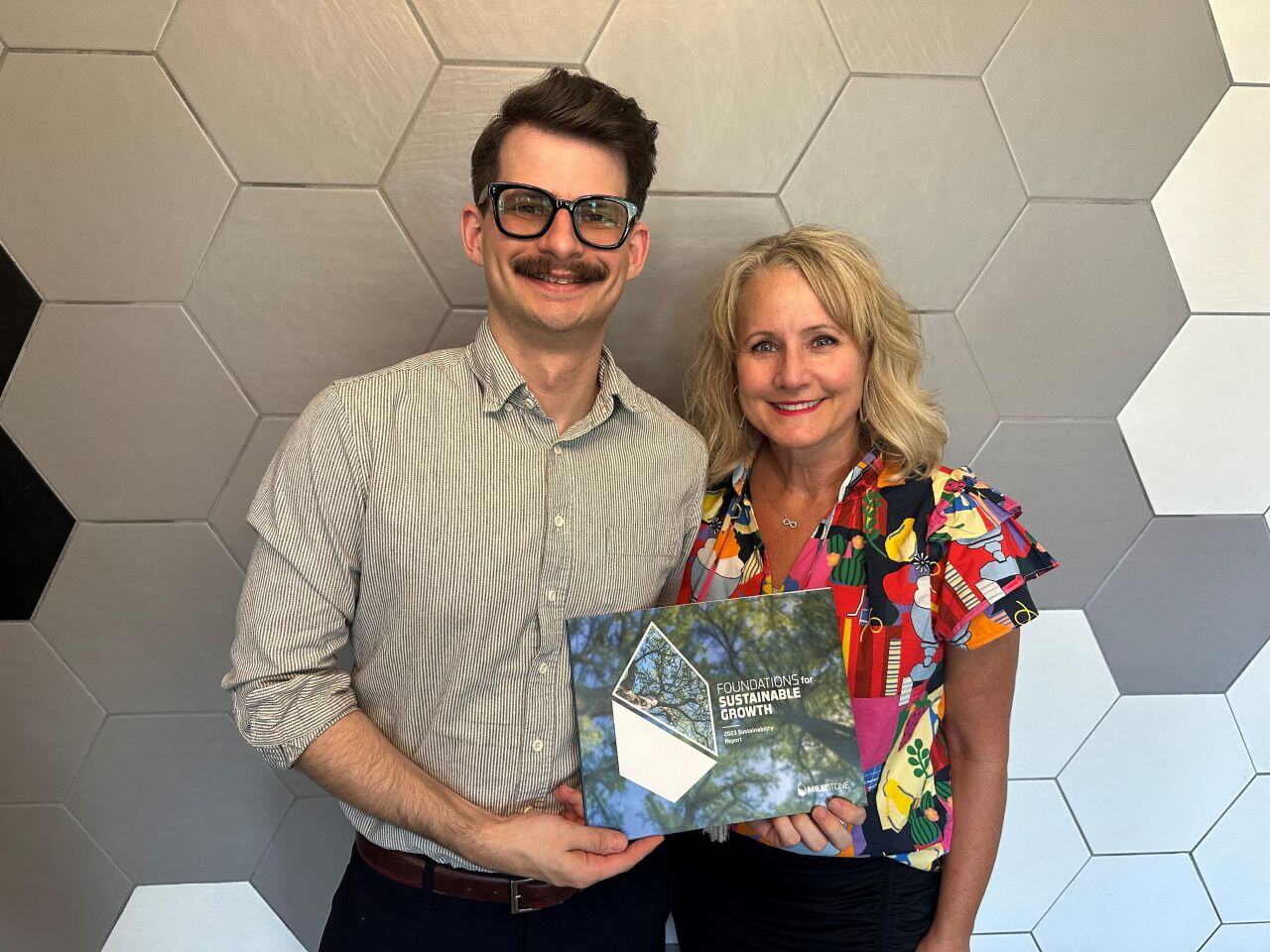 Garrett and Krista holding up a Milestone Sustainability Report designed by the BrandExtract team