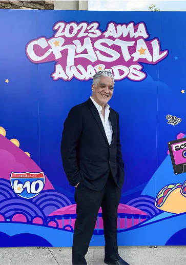 Adrian posing in front of the 2023 AMA Crystal Awards banner