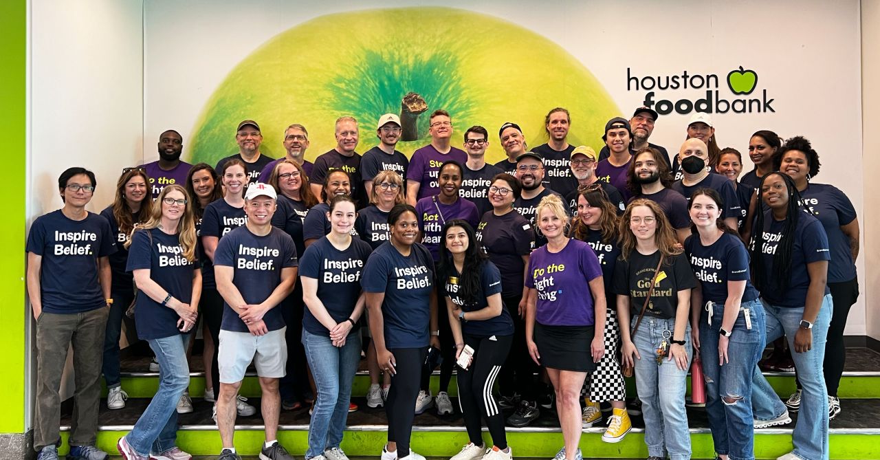 A photograph of the BrandExtract team standing in front of a wall at the Houston Food Bank.